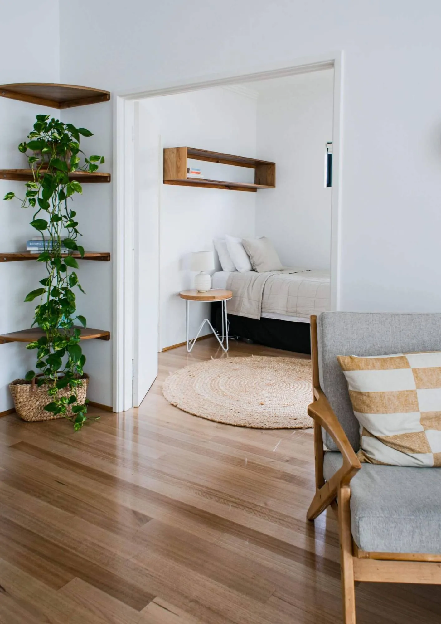 Freshly made bed seen through a doorway, with gleaming timber floors and a trailing plant