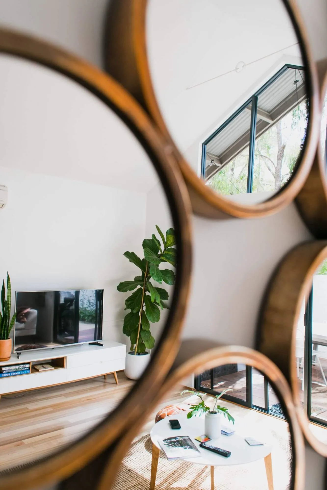 A spotless living room reflected in round timber-framed mirrors