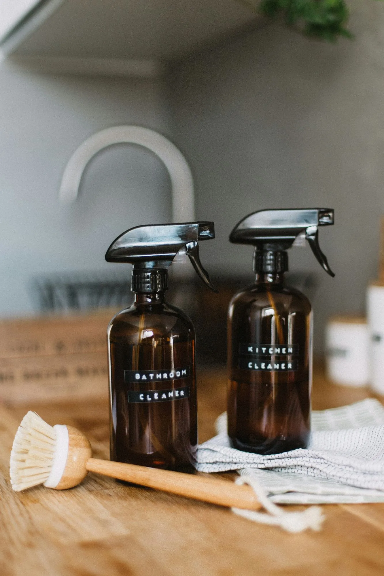 Amber glass spray bottles of natural bathroom and kitchen cleaner beside a wooden dish brush